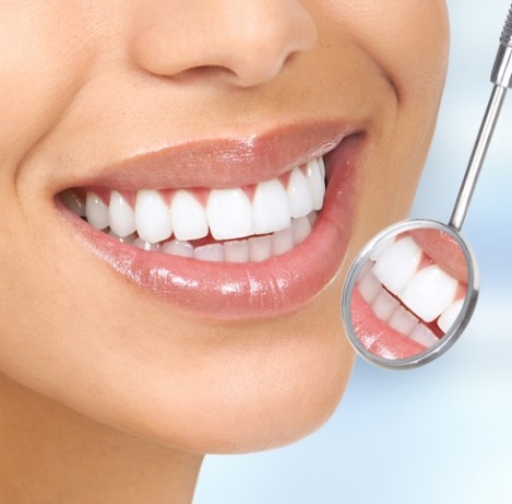 Close up of dental mirror reflecting smile with white teeth